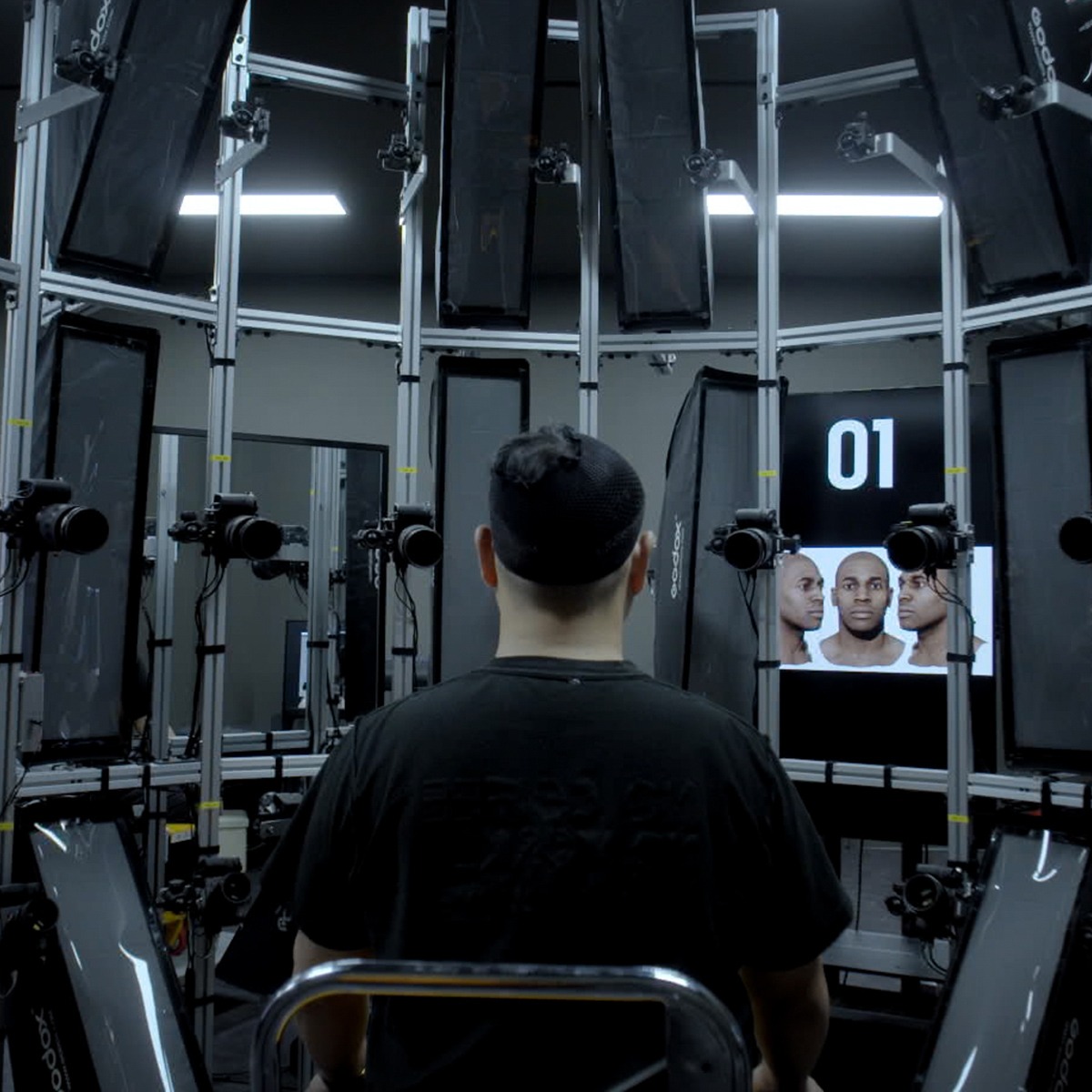 A man is sitting in a room with several monitors.